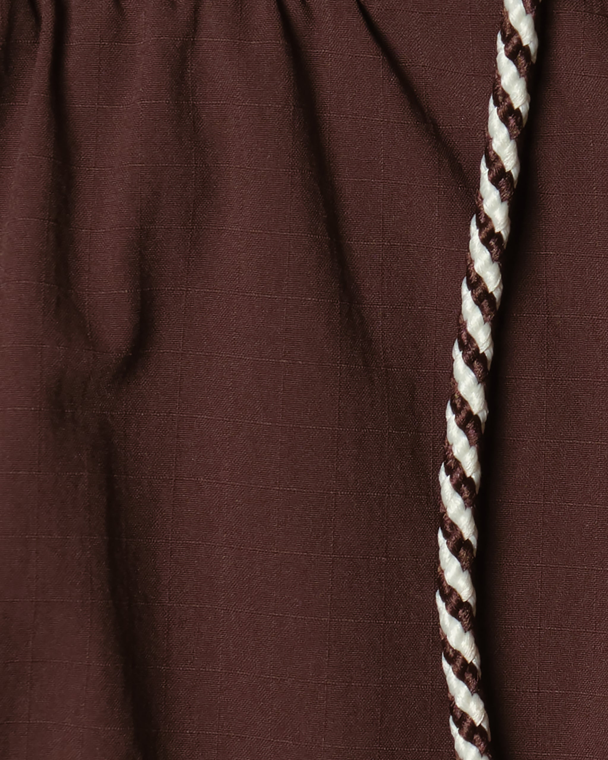 Close-up of textured brown fabric with a gathered seam and a twisted white/dark brown cord—detail from BEARDEDGOAT Men's Rambler Short, featuring 4-way stretch for trail running adventures.